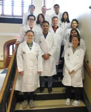 students in lab coats pose in stairwell