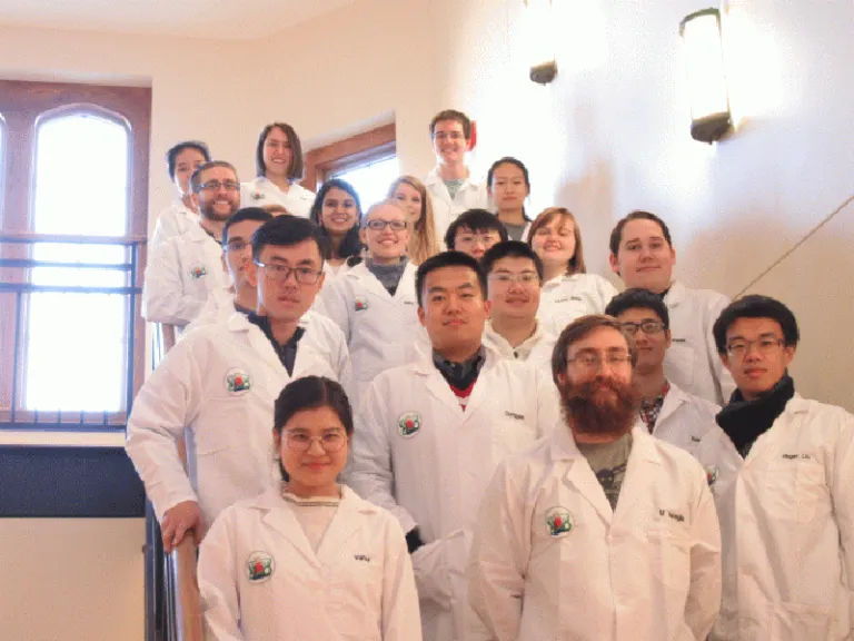 19 students in white lab coats stand on a staircase