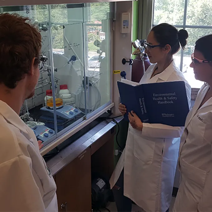 three people in lab coats look at lab equipment